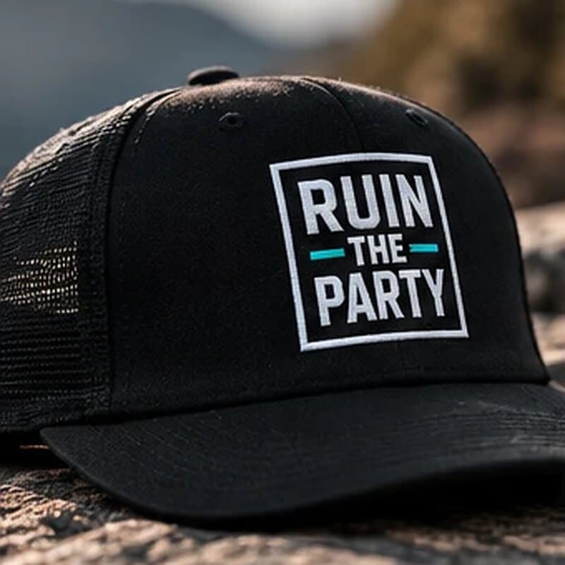 A black trucker cap with the boxed Ruin the Party patch, on a rock